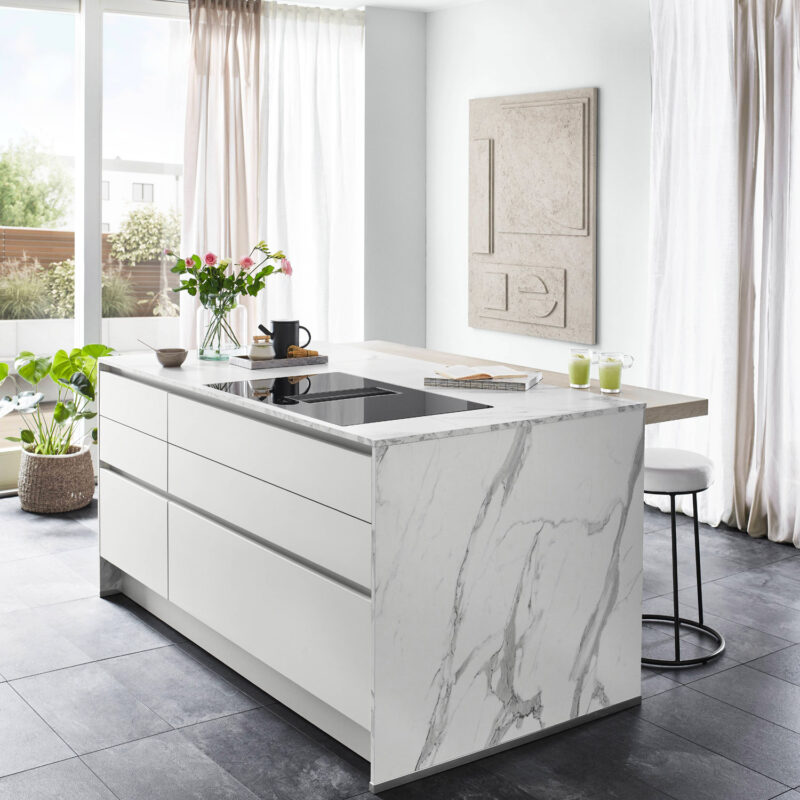 Cuisine moderne avec îlot central en marbre blanc, plan de cuisson intégré et tabourets de bar dans un intérieur lumineux
