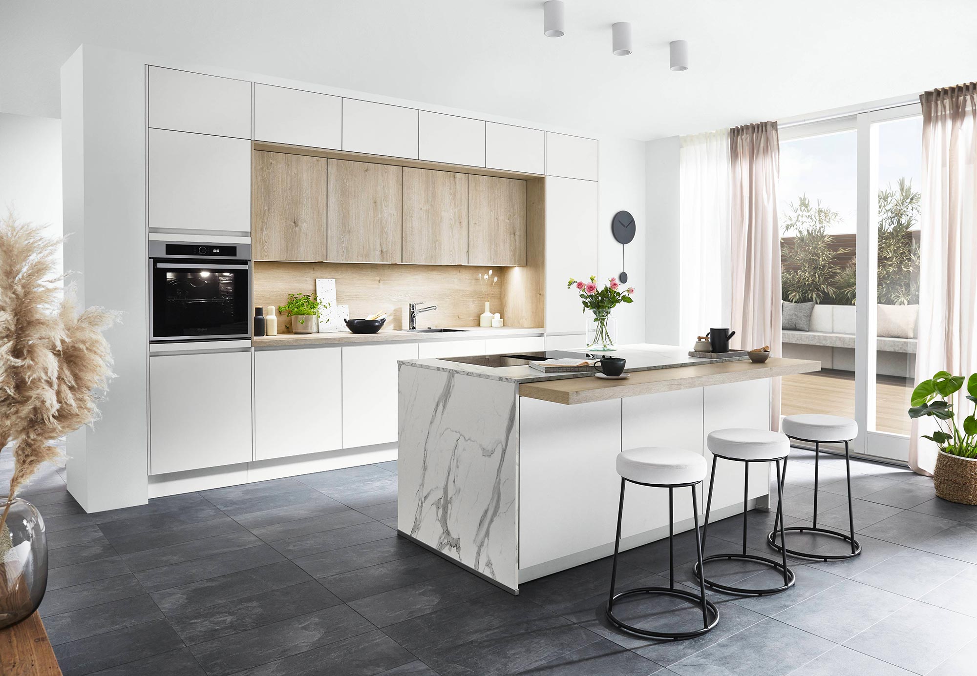 Cuisine moderne avec îlot central en marbre blanc, tabourets design et armoires bicolores blanc et bois naturel