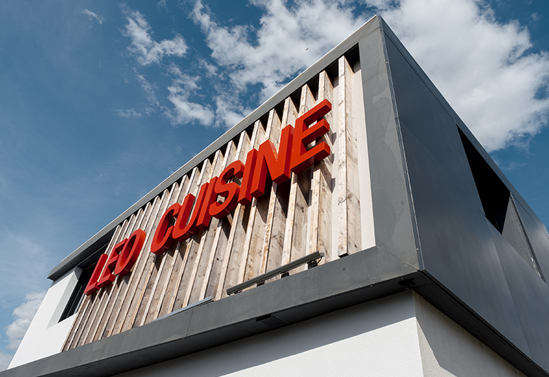 Bâtiment moderne avec enseigne rouge CUISINE sur façade blanche sous ciel bleu nuageux