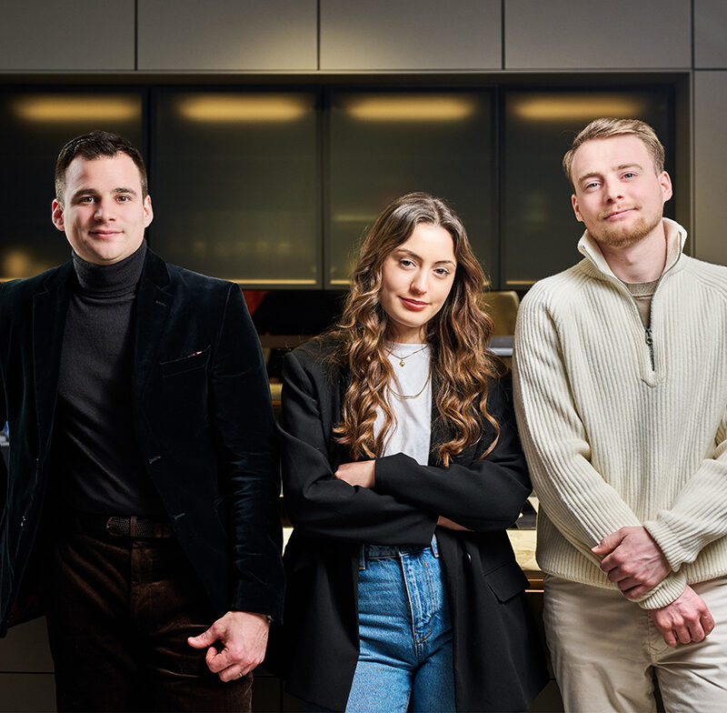Trois jeunes professionnels posent dans une cuisine moderne avec mobilier gris et plan de travail en bois