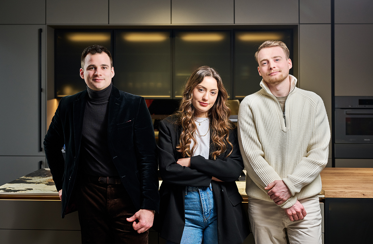 Trois jeunes professionnels posent dans une cuisine moderne avec mobilier gris et plan de travail en bois