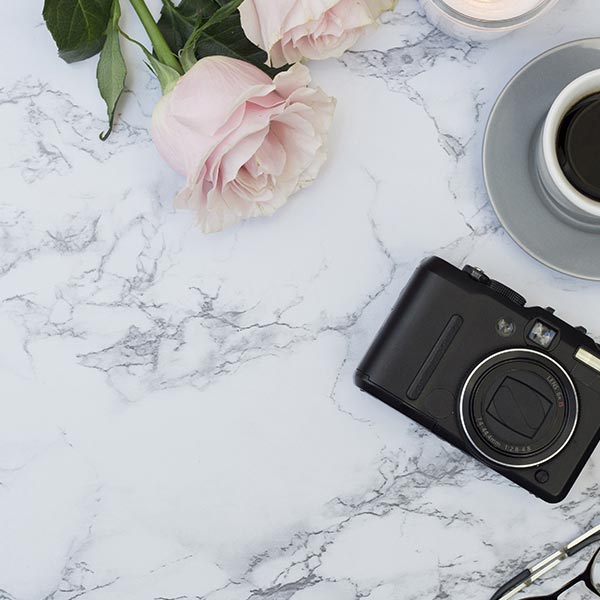 Appareil photo noir, tasse de café et roses roses disposés sur une surface en marbre blanc veiné de gris