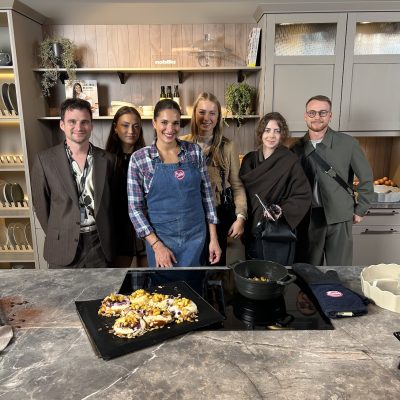 Groupe de six personnes posant dans une cuisine moderne après avoir préparé des plats sur une plaque de cuisson