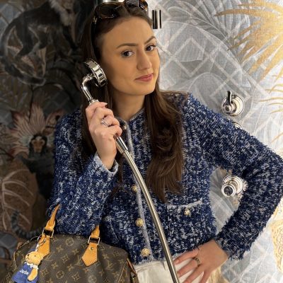 Femme élégante en veste bleue tweedée tenant une canne, avec sac Louis Vuitton dans une salle de bain luxueuse