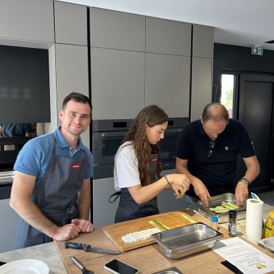 Trois personnes en tabliers cuisinent ensemble dans une cuisine moderne avec placards gris et équipements professionnels