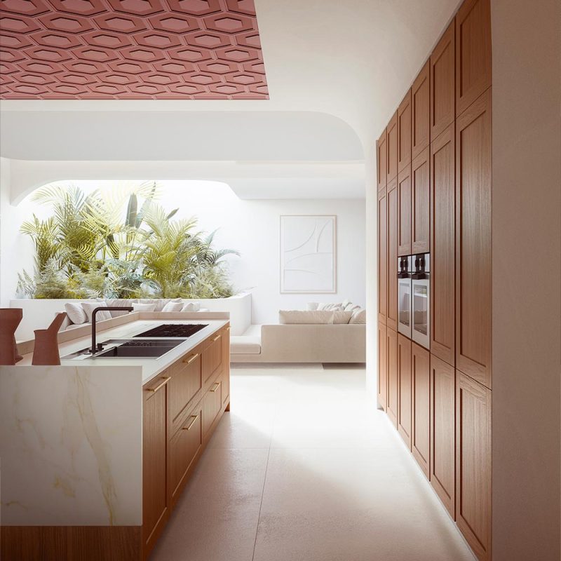 Cuisine moderne avec plafond hexagonal rose, îlot central blanc, armoires en bois et vue sur salon avec plantes