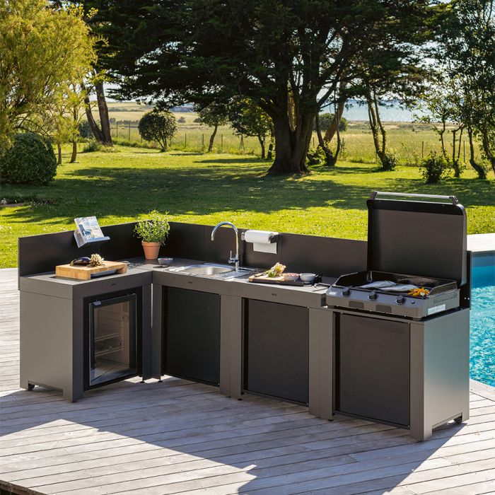 Cuisine d'extérieur moderne avec barbecue, évier et réfrigérateur sur terrasse face à un jardin verdoyant avec piscine