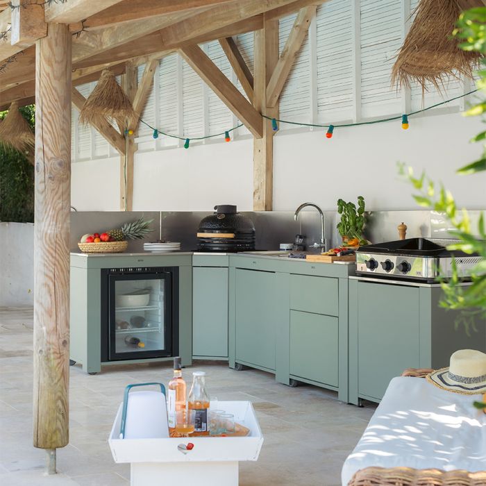 Cuisine extérieure moderne avec meubles verts sous pergola en bois, guirlandes lumineuses et réfrigérateur à boissons