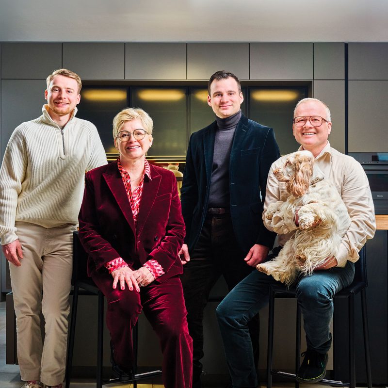 Quatre personnes souriantes posent dans une cuisine moderne, un homme tenant un petit chien aux poils longs et bouclés