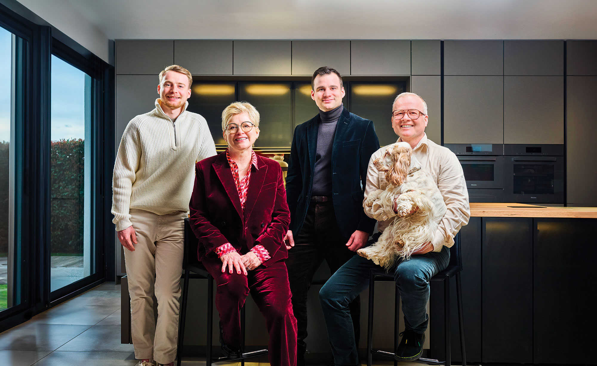 Quatre personnes souriantes posent dans une cuisine moderne, un homme tenant un petit chien aux poils longs et bouclés