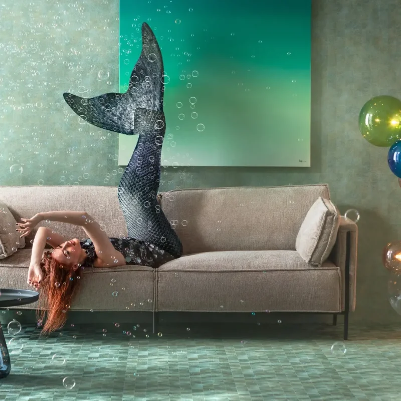 Femme avec queue de sirène allongée sur canapé beige dans salon aquatique avec bulles et luminaires colorés