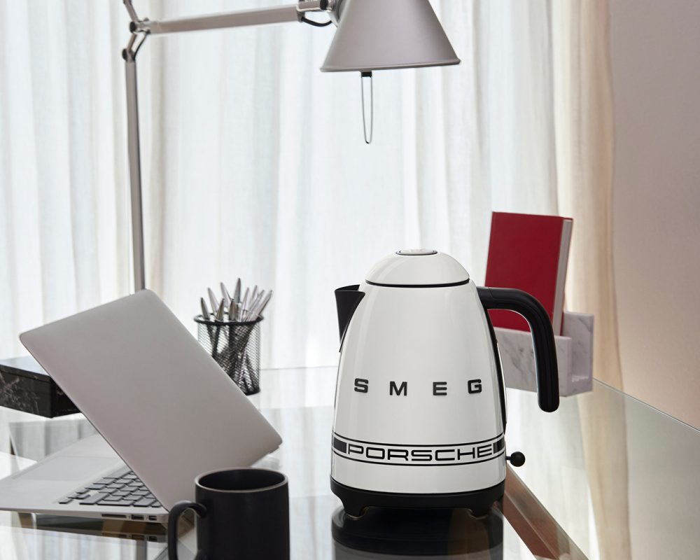 Bouilloire électrique blanche SMEG Porsche sur bureau moderne avec ordinateur portable et lampe articulée