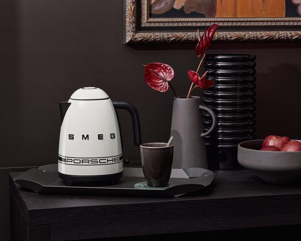 Bouilloire électrique SMEG Porsche blanche sur plateau noir avec tasse et plante décorative dans cuisine moderne