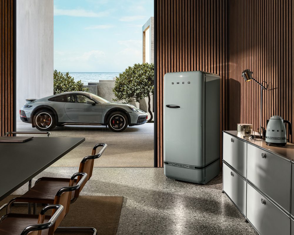 Cuisine moderne avec réfrigérateur Smeg gris, Porsche 911 garée dehors, vue sur mer et murs en bois