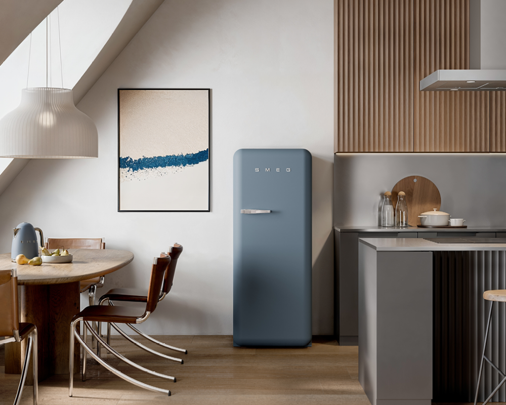 Cuisine moderne avec réfrigérateur bleu Smeg, îlot central gris, table ronde en bois et chaises design sous combles