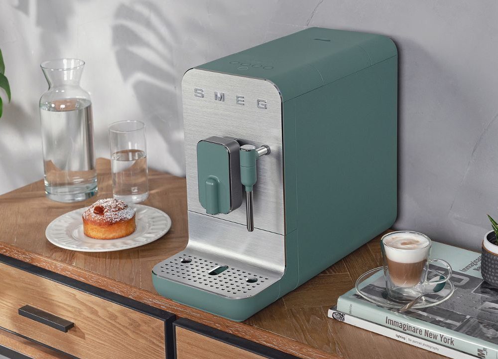 Machine à café SMEG verte sur meuble bois avec tasse cappuccino, donut et plantes décoratives dans cuisine moderne