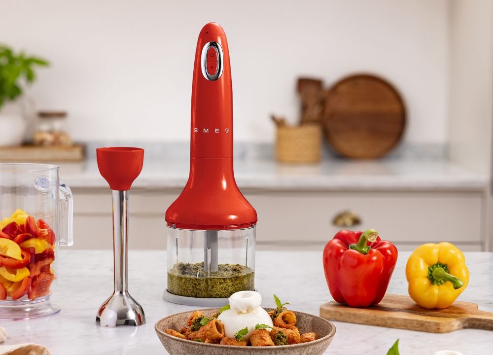 Mixeur plongeant rouge SMEG avec accessoires dans une cuisine moderne, légumes colorés et plat cuisiné sur plan de travail